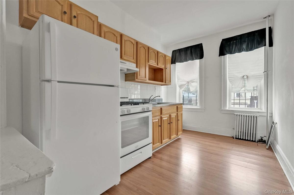 Kitchen featuring white appliances, radiator heating unit, tasteful backsplash, under cabinet range hood, and light wood-type flooring