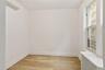 Empty room with radiator heating unit, light wood finished floors, and an AC wall unit