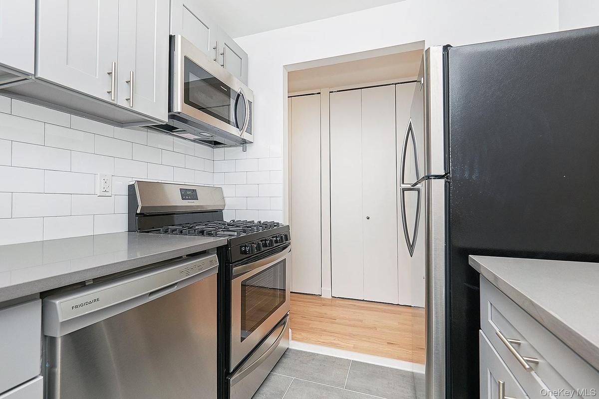 Kitchen featuring stainless steel appliances, tasteful backsplash, gray cabinets, light tile patterned floors, and light stone counters