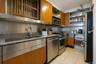 Kitchen featuring brown cabinets, dark stone counters, appliances with stainless steel finishes, light tile patterned flooring, and modern cabinets
