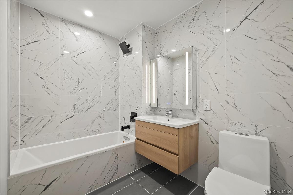 Full bathroom with tile walls, vanity, recessed lighting, and dark tile patterned flooring