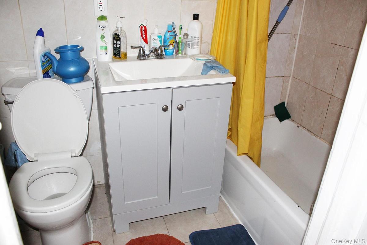 Bathroom featuring tile patterned flooring, shower / bath combo with shower curtain, vanity, and tile walls
