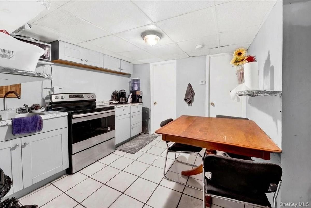 Kitchen featuring stainless steel electric stove, white cabinets, a drop ceiling, light countertops, and light tile patterned floors