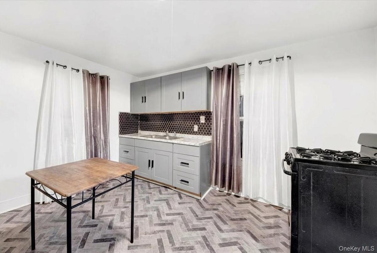 Kitchen with black gas range, gray cabinetry, light stone counters, and tasteful backsplash