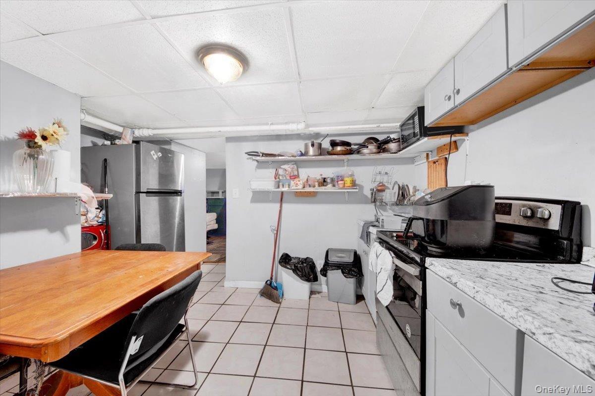 Kitchen with stainless steel appliances, light countertops, light tile patterned floors, white cabinets, and open shelves