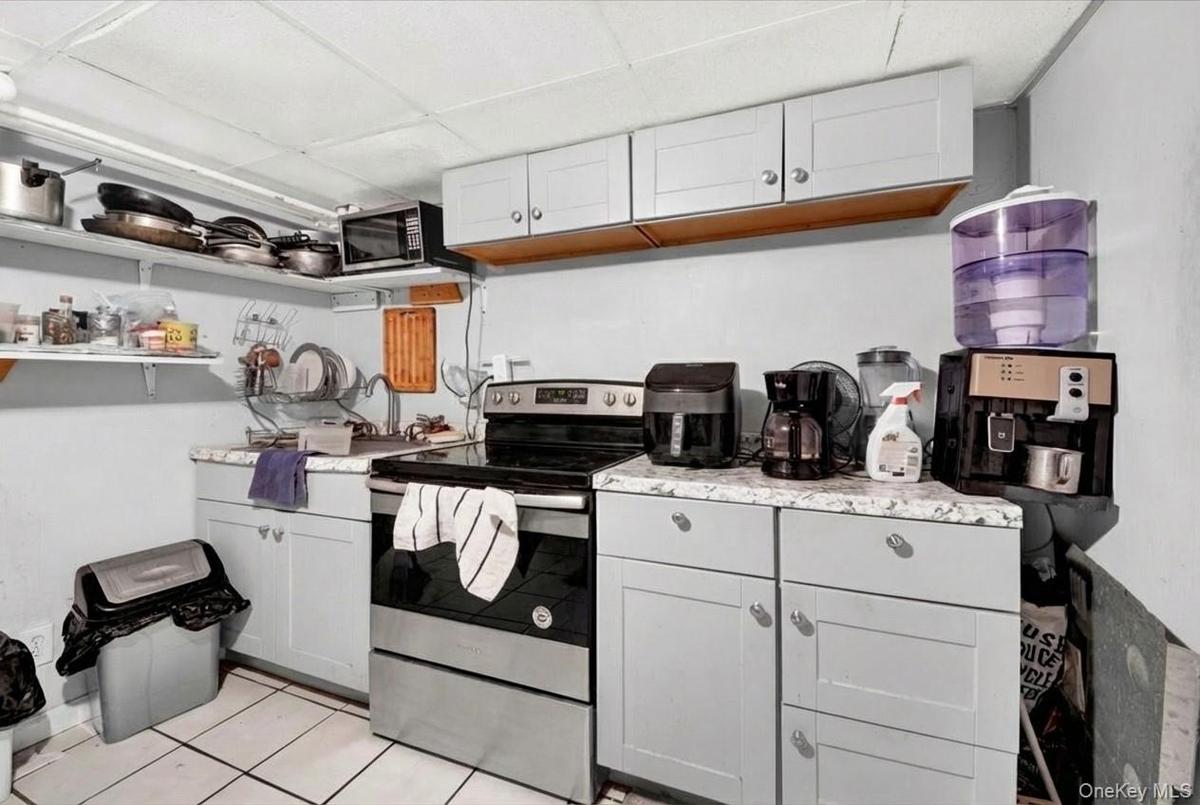Kitchen with stainless steel electric stove, white cabinets, open shelves, light tile patterned floors, and black microwave