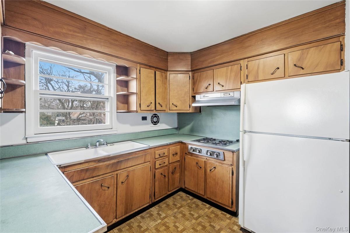Kitchen with open shelves, freestanding refrigerator, light countertops, and brown cabinetry