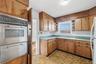Kitchen with open shelves, a warming drawer, light countertops, stainless steel oven, and brown cabinets