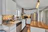 Kitchen with white cabinetry, wall chimney range hood, stainless steel appliances, light stone countertops, and hanging light fixtures