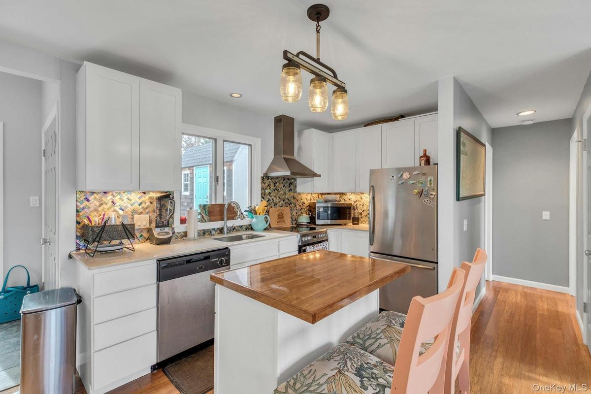 Kitchen featuring appliances with stainless steel finishes, wall chimney exhaust hood, white cabinets, decorative light fixtures, and butcher block co