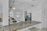 Kitchen featuring white cabinets, light stone counters, decorative light fixtures, glass insert cabinets, and stainless steel fridge with ice dispense