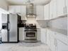 Kitchen with appliances with stainless steel finishes, light marble finish floors, wall chimney exhaust hood, and white cabinetry