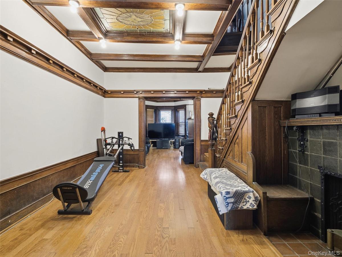 Exercise room featuring a wainscoted wall, wood walls, coffered ceiling, light wood-type flooring, and a fireplace