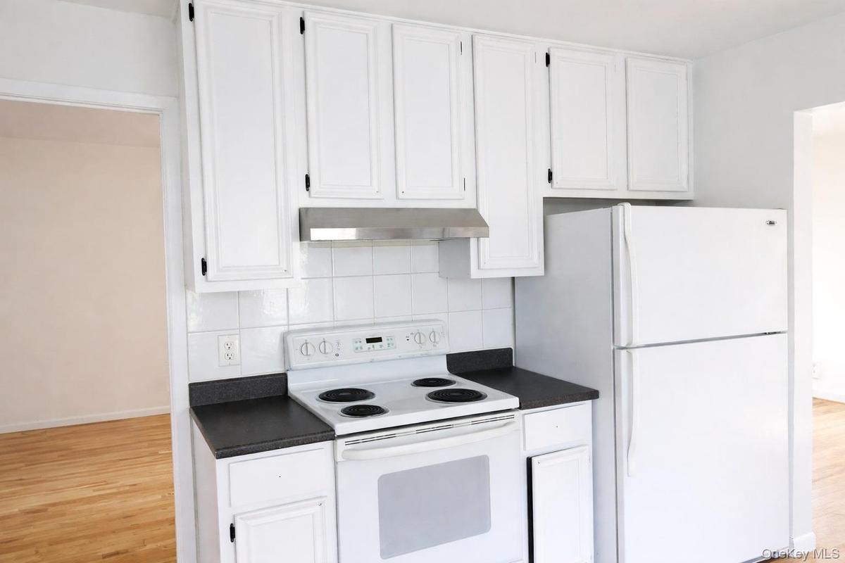 Kitchen featuring white appliances, dark countertops, white cabinetry, and light wood-style flooring
