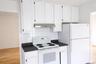 Kitchen featuring white appliances, dark countertops, white cabinetry, and light wood-style flooring
