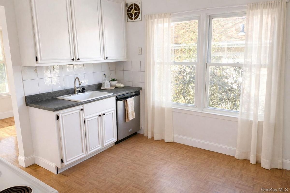 Kitchen featuring white cabinetry, dark countertops, stainless steel dishwasher, and decorative backsplash