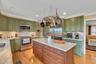 Kitchen with green cabinetry, crown molding, stainless steel appliances, light stone countertops, and a kitchen island