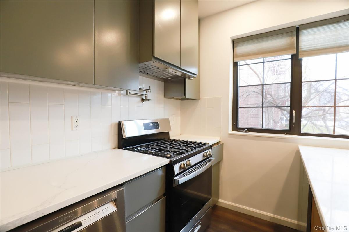 Kitchen featuring appliances with stainless steel finishes, sage green cabinetry, light stone counters, backsplash, and under cabinet range hood