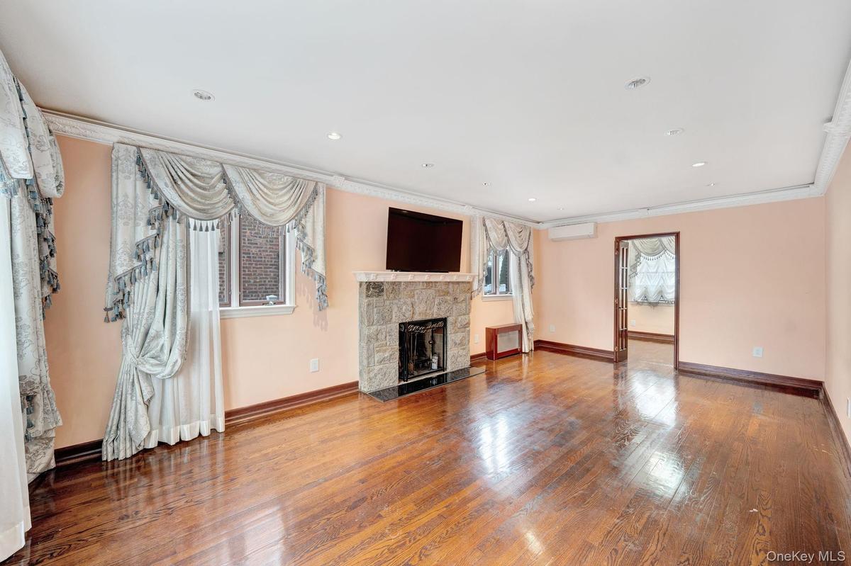 Unfurnished living room featuring a stone fireplace, hardwood / wood-style flooring, recessed lighting, ornamental molding, and an AC wall unit
