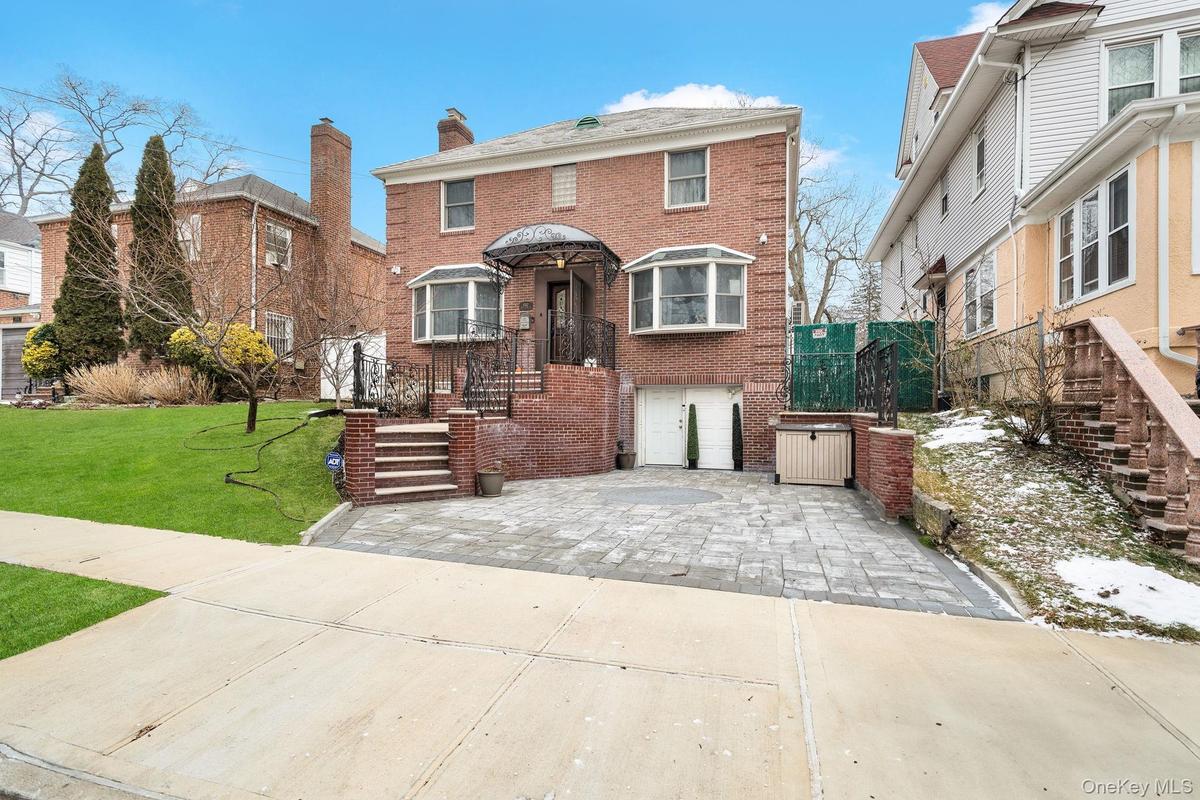 View of front facade featuring brick siding, a front lawn, an attached garage, driveway, and a chimney