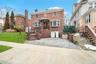 View of front facade featuring brick siding, a front lawn, an attached garage, driveway, and a chimney