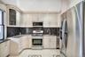 Kitchen with stainless steel appliances, dark stone countertops, light tile patterned flooring, glass insert cabinets, and tasteful backsplash