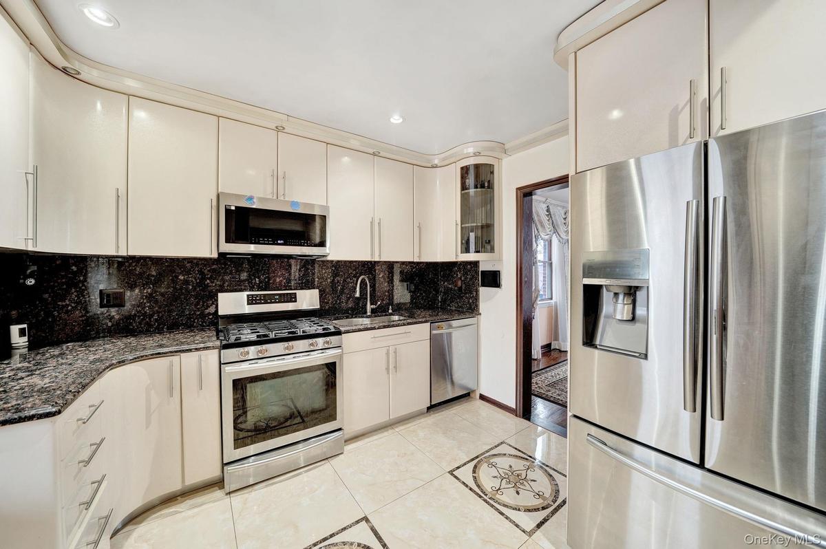 Kitchen featuring stainless steel appliances, dark stone counters, glass insert cabinets, light tile patterned floors, and decorative backsplash