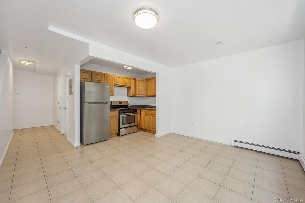 Kitchen featuring appliances with stainless steel finishes, dark countertops, a baseboard heating unit, brown cabinetry, and light tile patterned floo