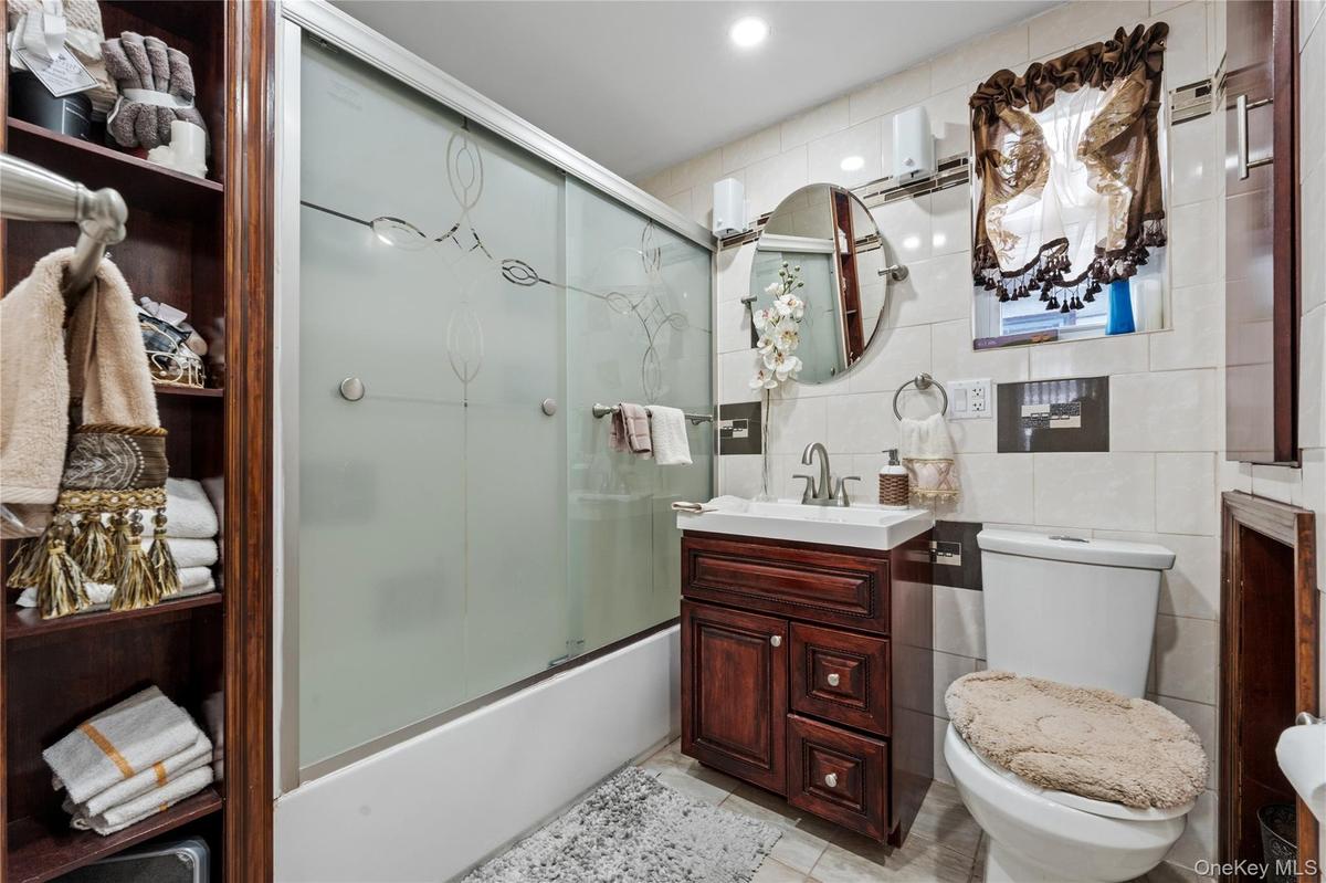 Full bath featuring tile walls, enclosed tub / shower combo, and vanity