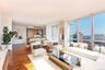 Living area featuring dark wood-type flooring, a view of city, expansive windows, and baseboards