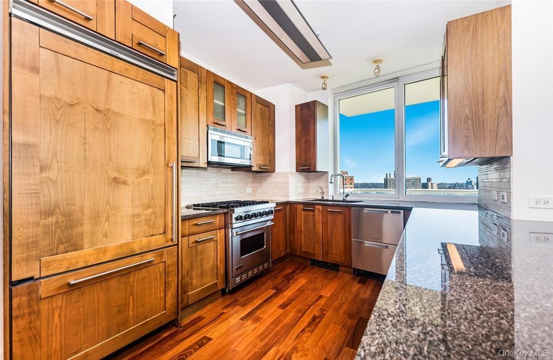 Kitchen featuring dark stone countertops, dark hardwood / wood-style flooring, decorative backsplash, high quality appliances, and sink