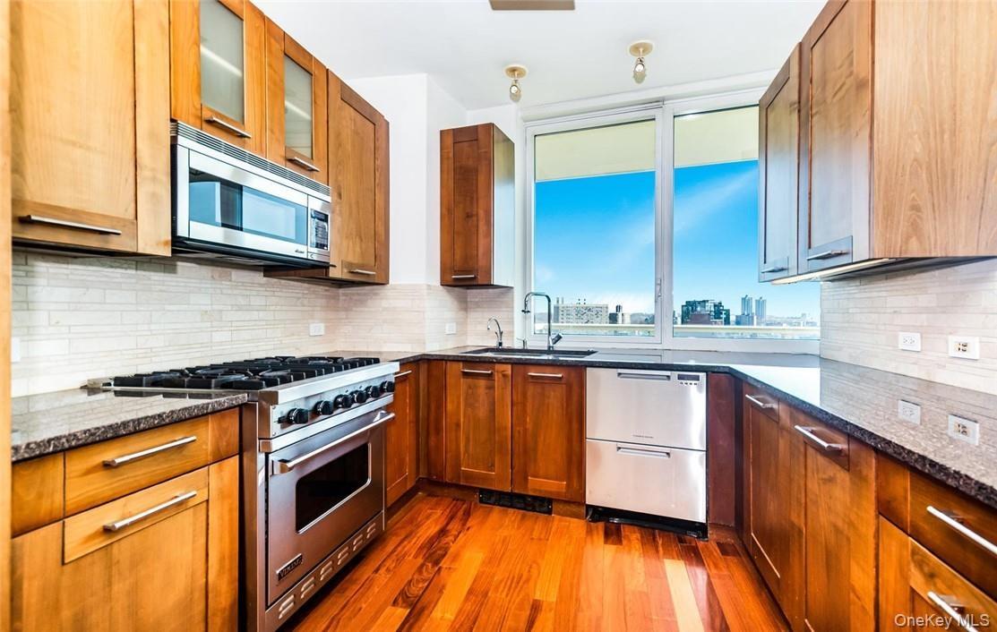 Kitchen with appliances with stainless steel finishes, dark hardwood / wood-style flooring, decorative backsplash, and sink