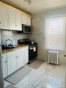 Kitchen with white cabinets, appliances with stainless steel finishes, wood counters, radiator heating unit, and light marble finish floors