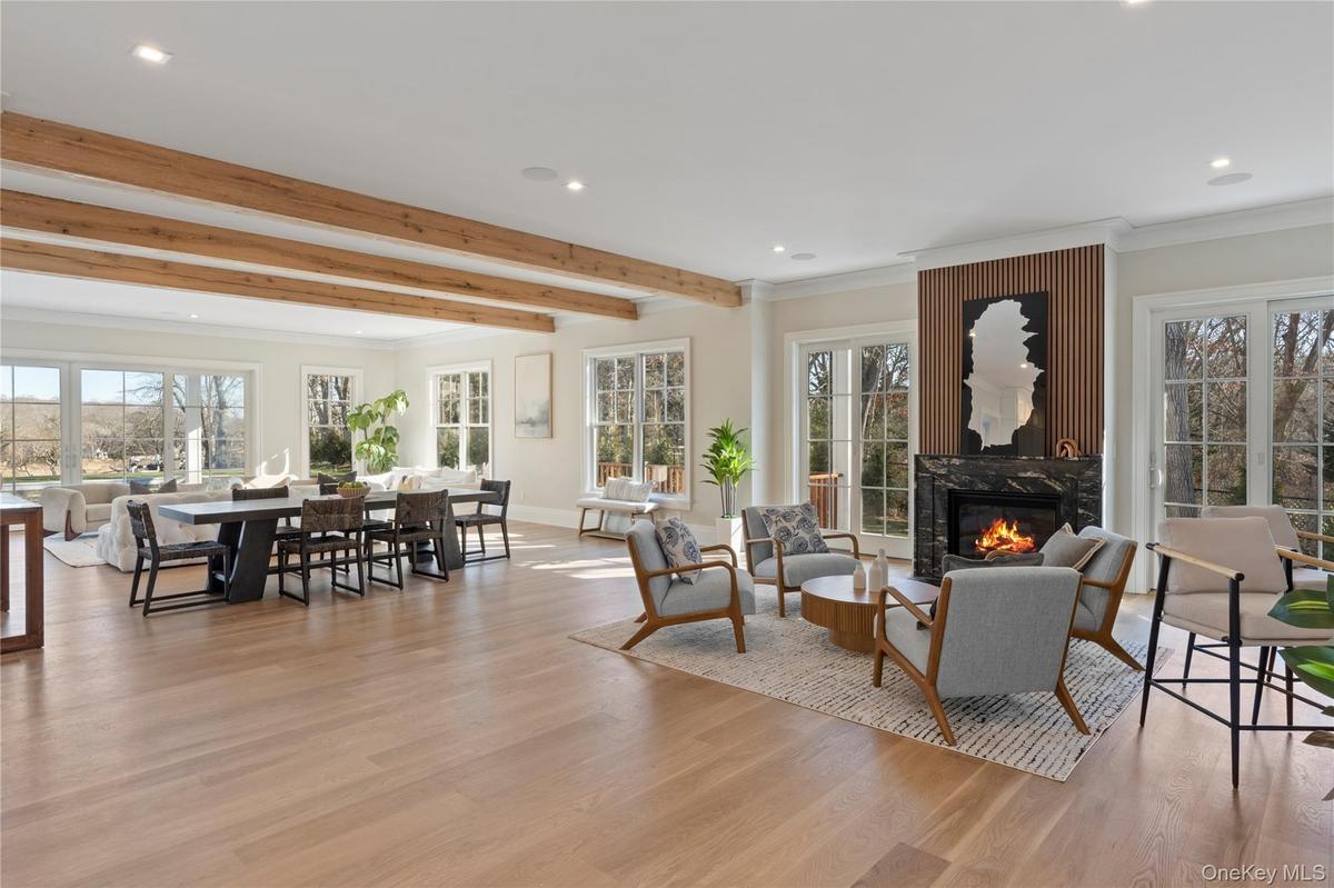 A dramatic great room with soaring ceilings, wide plank white oak floors, and walls windows framing panoramic waterfront vistas