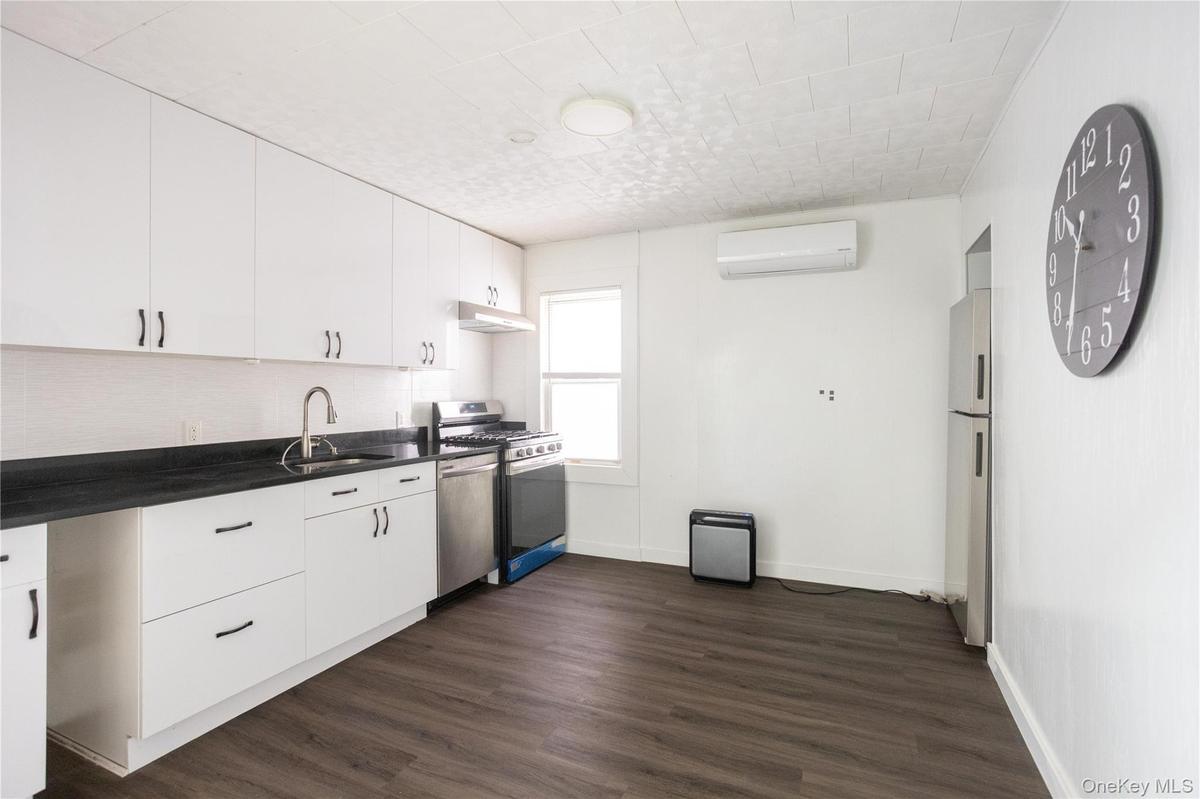 Kitchen with white cabinets, stainless steel appliances, dark wood-style floors, and a wall mounted air conditioner