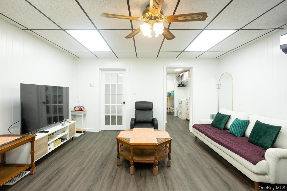 Living room featuring a drop ceiling, ceiling fan, and dark wood-style flooring