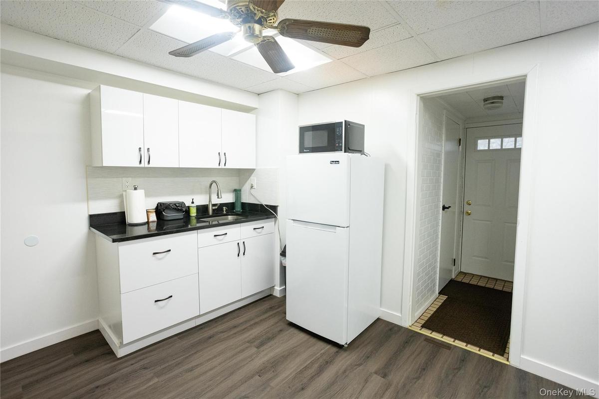 Kitchen featuring dark countertops, freestanding refrigerator, white cabinets, a paneled ceiling, and black microwave