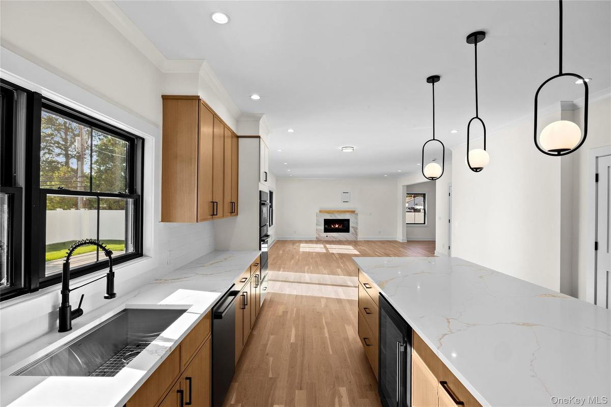 Kitchen with light wood finished floors, light stone countertops, a warm lit fireplace, open floor plan, and beverage cooler