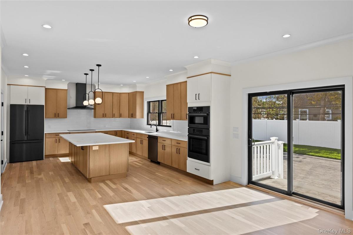 Kitchen featuring black appliances, light wood-style floors, pendant lighting, a kitchen island, and tasteful backsplash