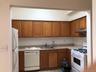 Kitchen featuring white appliances, brown cabinets, light countertops, under cabinet range hood, and light tile patterned floors