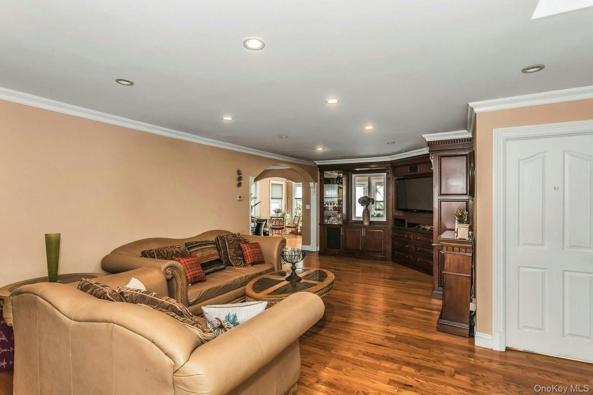 Living area with arched walkways, dark wood-style flooring, recessed lighting, and crown molding