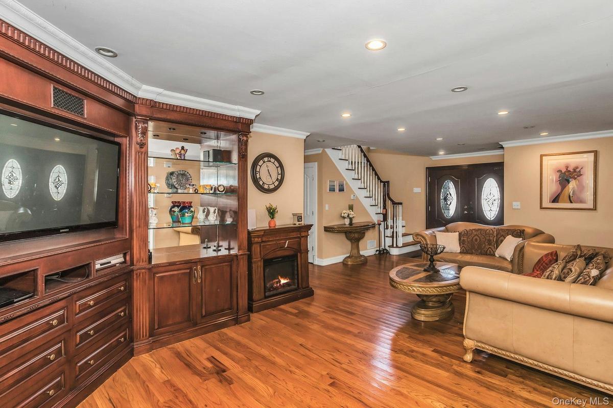 Living room featuring ornamental molding, dark wood finished floors, stairs, a glass covered fireplace, and recessed lighting