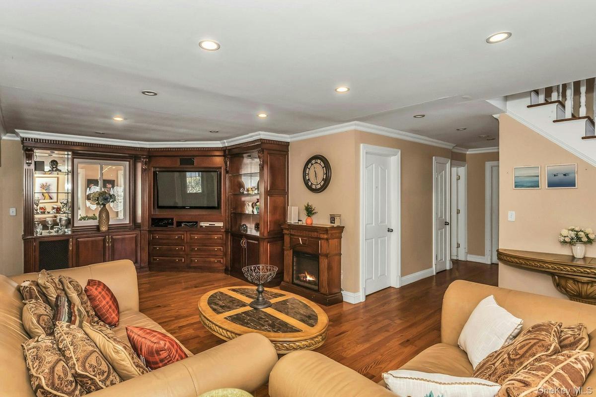 Living area featuring a glass covered fireplace, wood finished floors, crown molding, stairs, and recessed lighting