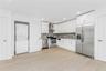 Kitchen with stainless steel appliances, wall chimney range hood, estacked washer and dryer, light wood-style floors, and backsplash