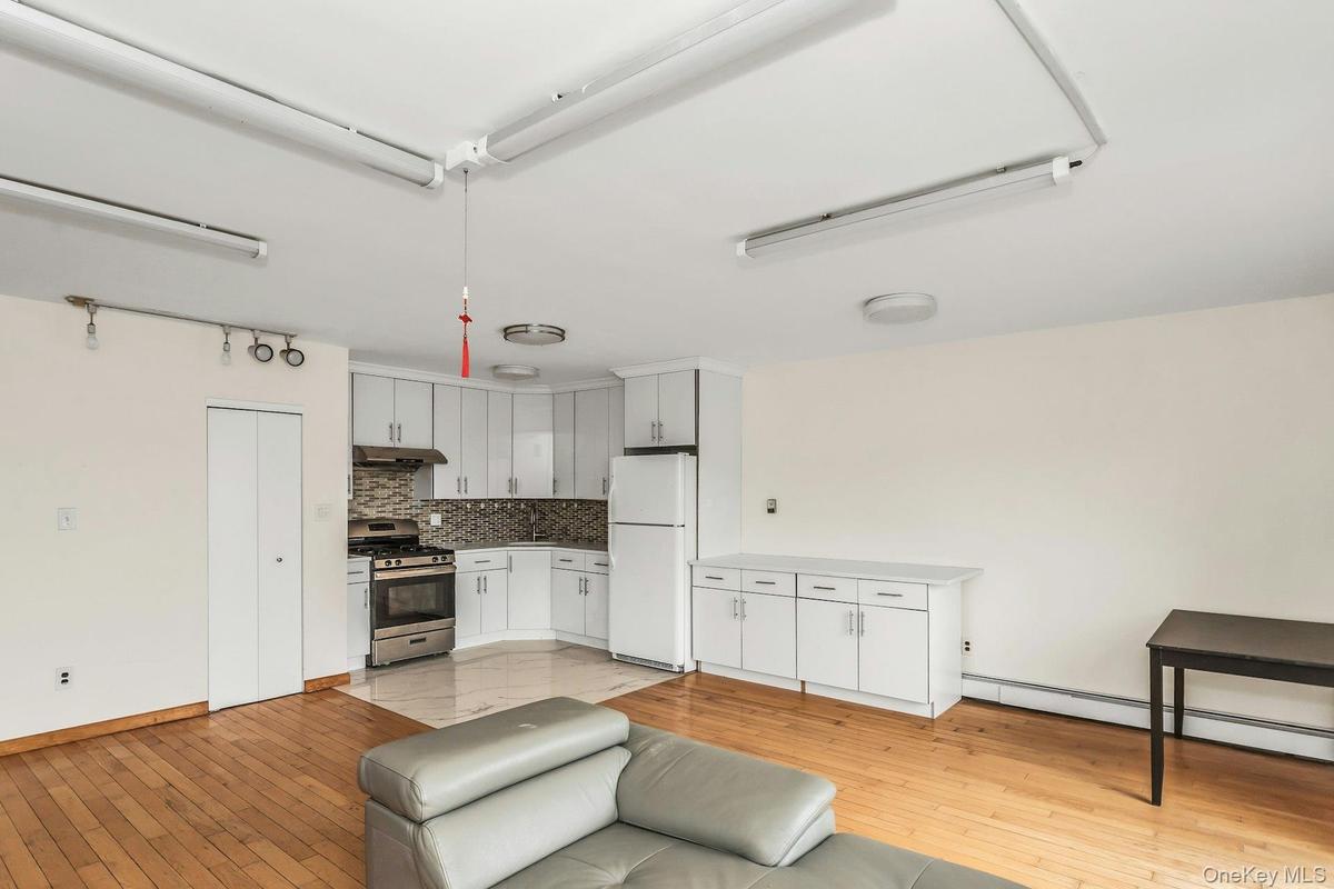 Kitchen with white cabinetry, freestanding refrigerator, stainless steel gas range oven, light wood-type flooring, and baseboard heating