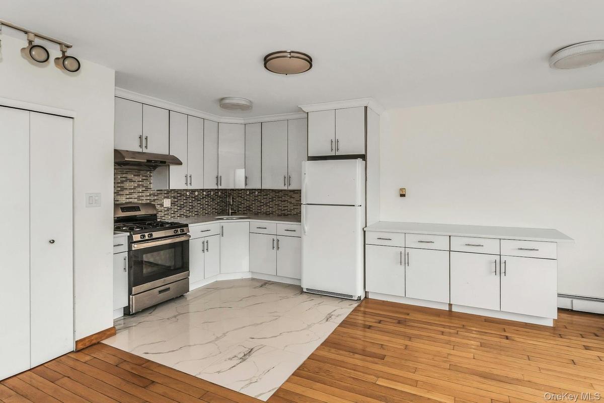 Kitchen with light wood-style flooring, freestanding refrigerator, stainless steel gas range oven, white cabinetry, and under cabinet range hood