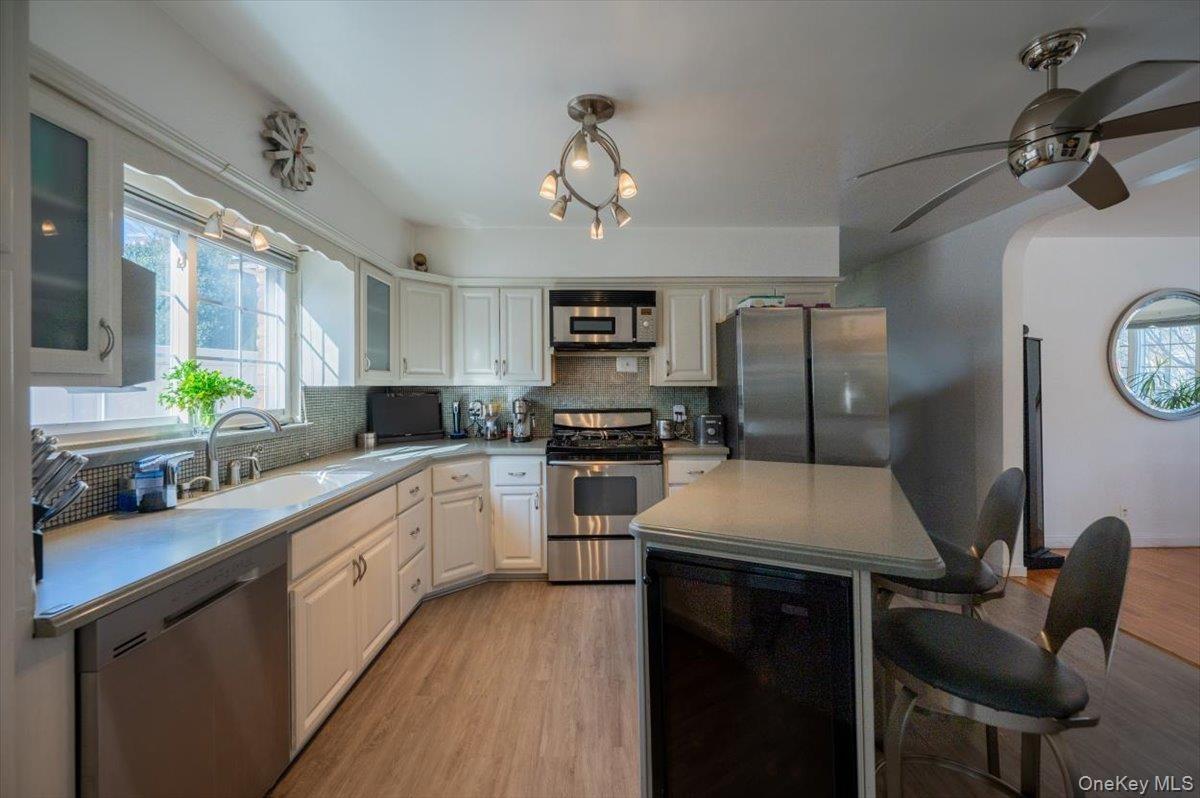 Kitchen featuring appliances with stainless steel finishes, a breakfast bar area, backsplash, light wood finished floors, and glass insert cabinets