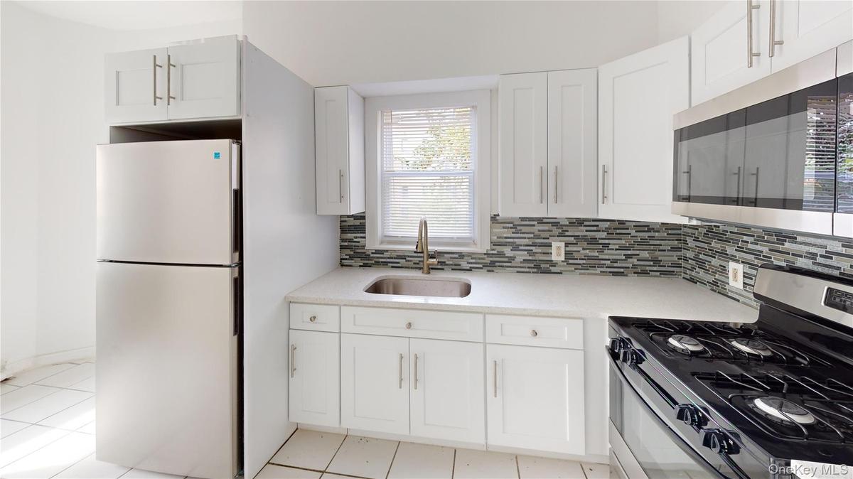 Kitchen with stainless steel appliances, white cabinets, light stone countertops, decorative backsplash, and light tile patterned flooring