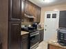 Kitchen with stainless steel appliances, tasteful backsplash, under cabinet range hood, light stone countertops, and dark brown cabinetry