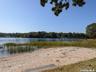 Sandy waterfront featuring a wooden bench, marsh grass, and a distant pier